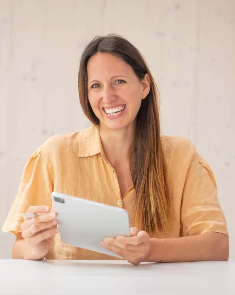 Das Bild zeigt Tatiana Karcher, wie sie dich an einem Schreibtisch sitzend mit ihrem iPad in der Hand anlächelt.