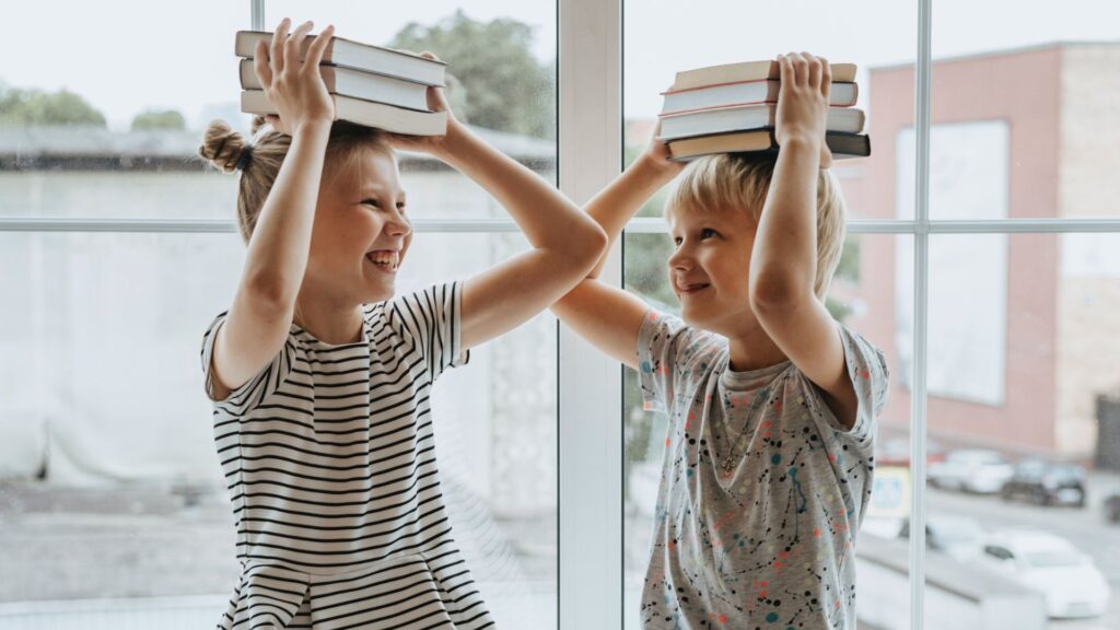 Die (negativen) Folgen von Schule (Newsletter 3/2025) 3 Zwei Schüler, die im Chaos des Klassenraums Bücher auf dem Kopf balancieren