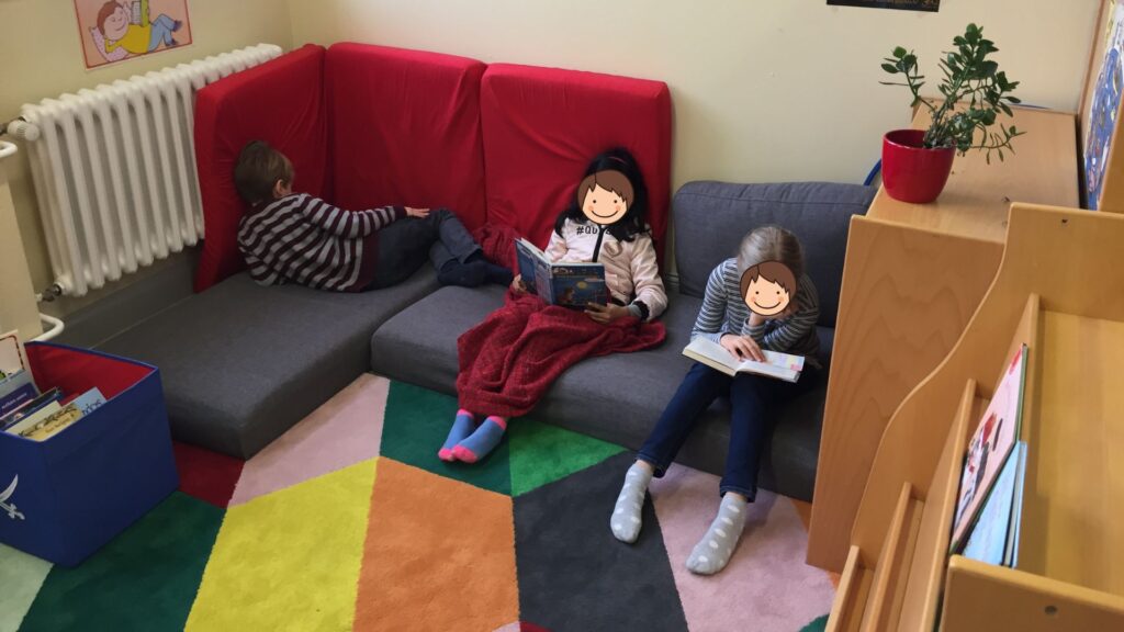 12 bewährte Rituale in der Grundschule: So schaffst du eine strukturierte und entspannte Lernumgebung 5 Ein Blick in die Leseecke im hinteren Bereich des Klassenraumes, in dem 3 Kinder entspannt lesen.